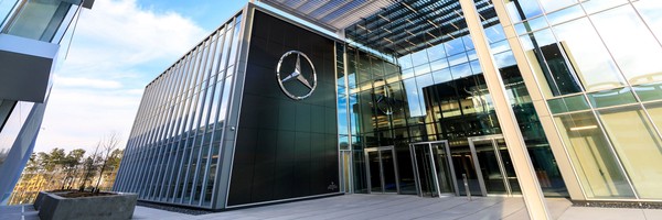 Modernes Gebäude mit Glasfassade und großem Mercedes-Logo bei sonnigem Wetter.