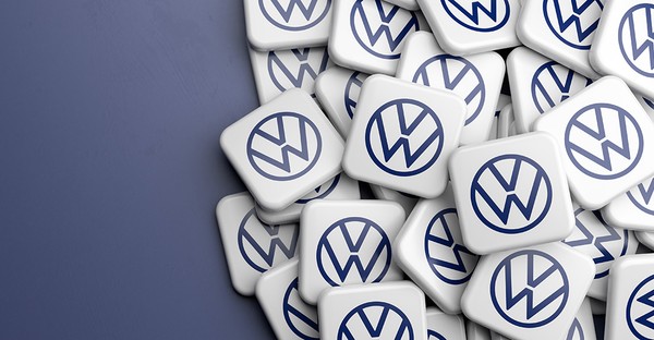 Viele VW-Logos auf weißen quadratischen Plaketten, die auf einer blauen Fläche liegen.