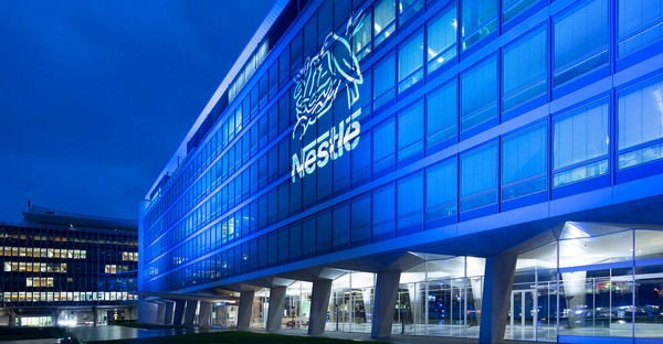 Modernes Gebäude mit blau beleuchteter Glasfassade und großem Logo bei Nacht.