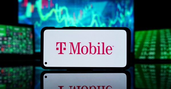 Smartphone mit T-Mobile-Logo, im Hintergrund unscharfe Börsenbildschirme.
