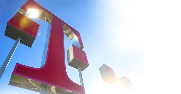 Großes, rotes T-Logo vor blauem Himmel mit Sonnenstrahlen im Hintergrund.