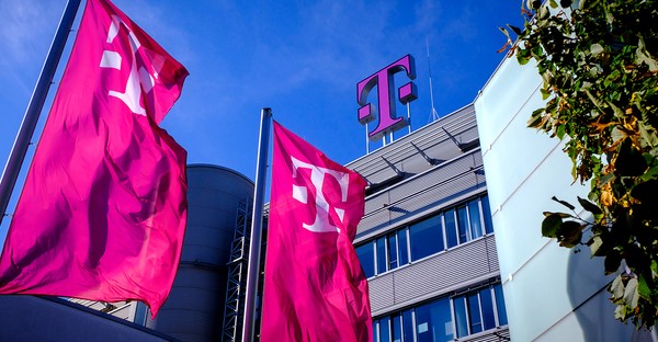 Gebäude mit Telekom-Logo und rosa Fahnen, blauer Himmel im Hintergrund.