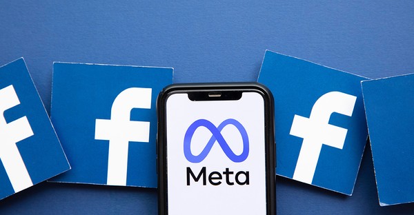 Smartphone mit Meta-Logo, umgeben von Facebook-Logos auf blauem Hintergrund.