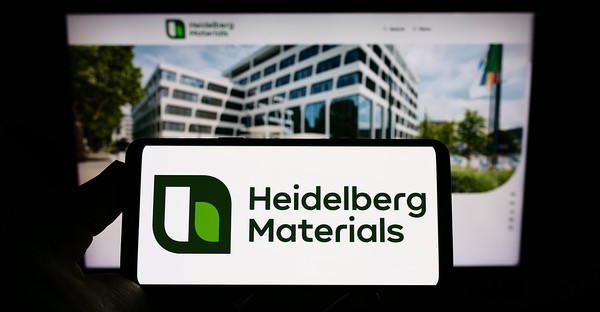 Smartphone mit Heidelberg Materials Logo vor unscharfem Bürogebäude im Hintergrund.