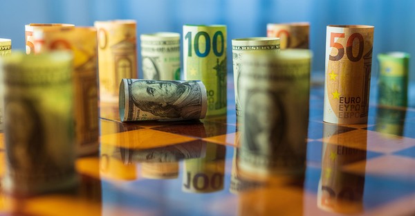 Gerollte Euro- und Dollar-Scheine stehen auf einem Schachbrett.