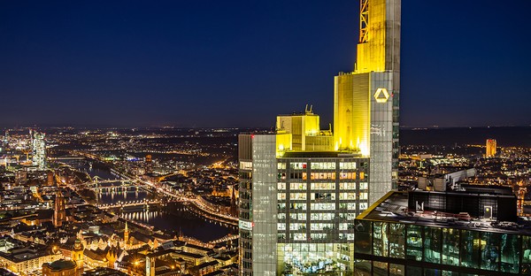 Frankfurter Skyline bei Nacht mit beleuchtetem Hochhaus und Fluss im Hintergrund.