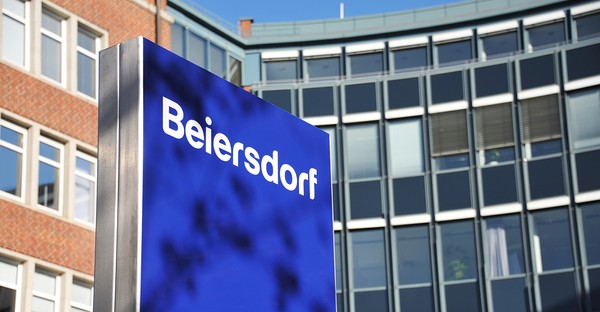 Blaues Schild mit "Beiersdorf" vor modernen Bürogebäuden.