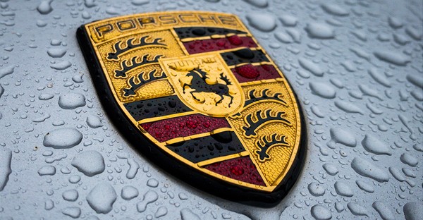 Porsche-Logo auf nasser Oberfläche mit Wassertropfen.