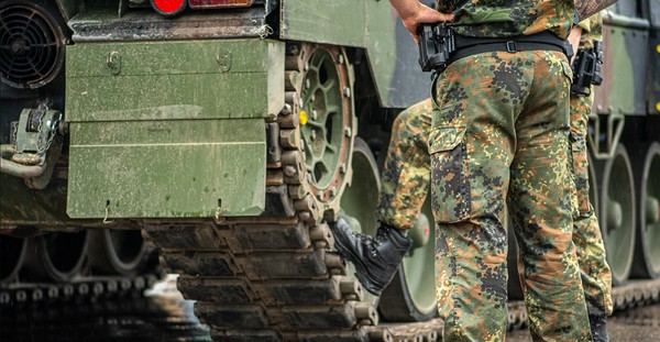 Zwei deutsche Soldaten in Tarnuniform stehen während einer Pause vor einem Panzer.