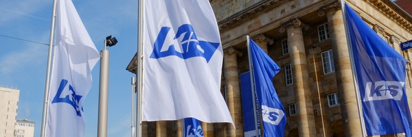 Weiße und blaue Fahnen mit K+S-Logo wehen vor einem historischen Gebäude mit Säulen.