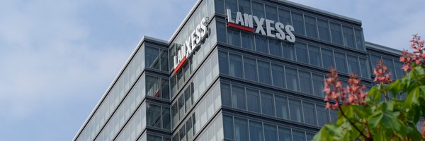 Glasgebäude mit Lanxess-Logo, blauer Himmel und Baum im Vordergrund.