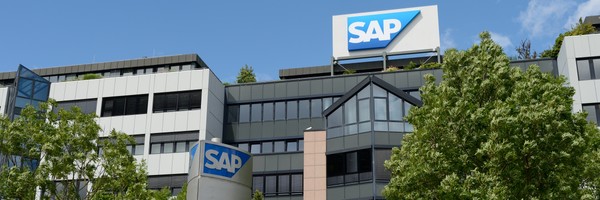 Gebäude mit SAP-Logos, umgeben von Bäumen, unter blauem Himmel.