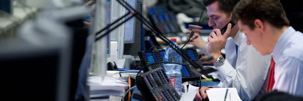 Männer arbeiten in einem Büro mit Computern und Telefonen, konzentriert auf Bildschirme.