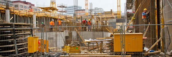 Bauarbeiter auf einer großen Baustelle mit Kränen und Gebäuden im Hintergrund.