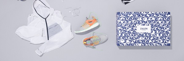 Weiße Jacke, bunte Sneaker und Zalon-Box auf grauem Hintergrund.