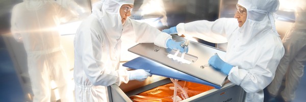 Zwei Personen in Schutzanzügen arbeiten an einem Behälter in einem Labor.