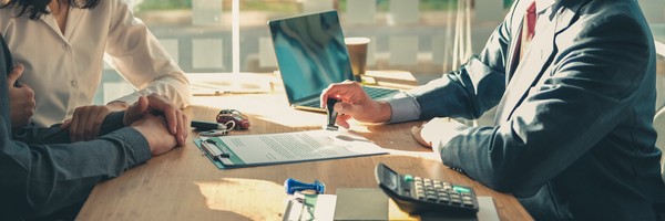Personen im Gespräch an einem Tisch mit Dokumenten, Laptop und Taschenrechner.