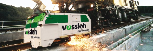 Maschine von Vossloh schleift Schienen und erzeugt Funken auf einer Eisenbahnstrecke.