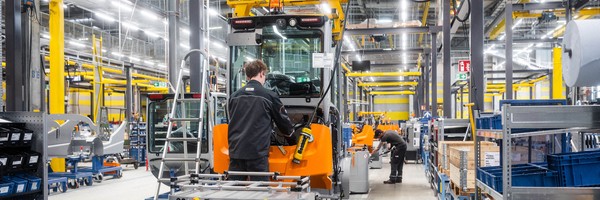 Personen arbeiten in einer hellen Fabrikhalle an großen Maschinen.